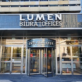 Wejście do biurowca Lumen przy ulicy Emilii Plater z obrotowymi drzwiami i szklaną fasadą.