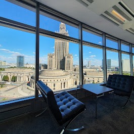 Wnętrze biura z panoramicznym widokiem na Pałac Kultury i Nauki w Warszawie, czarne skórzane fotele Barcelona i stolik kawowy na pierwszym planie, duże okna od podłogi do sufitu.