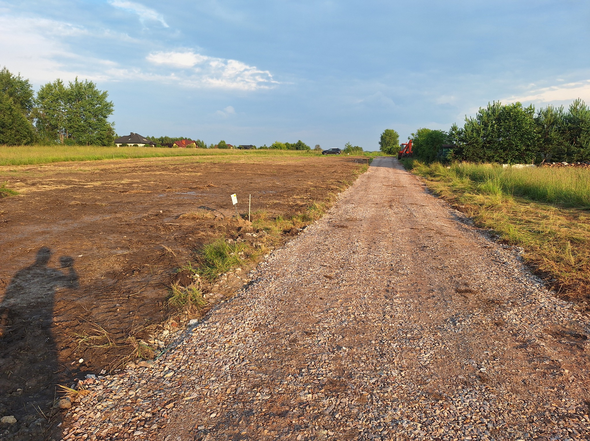 Droga gruntowa utwardzona kruszywem w Miedzianej Górze, obok przygotowany teren pod budowę, w tle zabudowa jednorodzinna i cień dwóch osób.