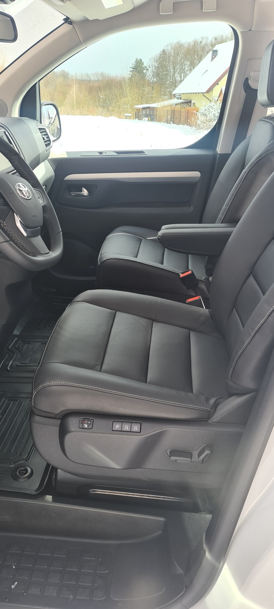 Wnętrze samochodu z czarną skórzaną tapicerką, widoczne fotele z regulacją elektryczną i podłokietnikiem, na zewnątrz zimowy krajobraz.