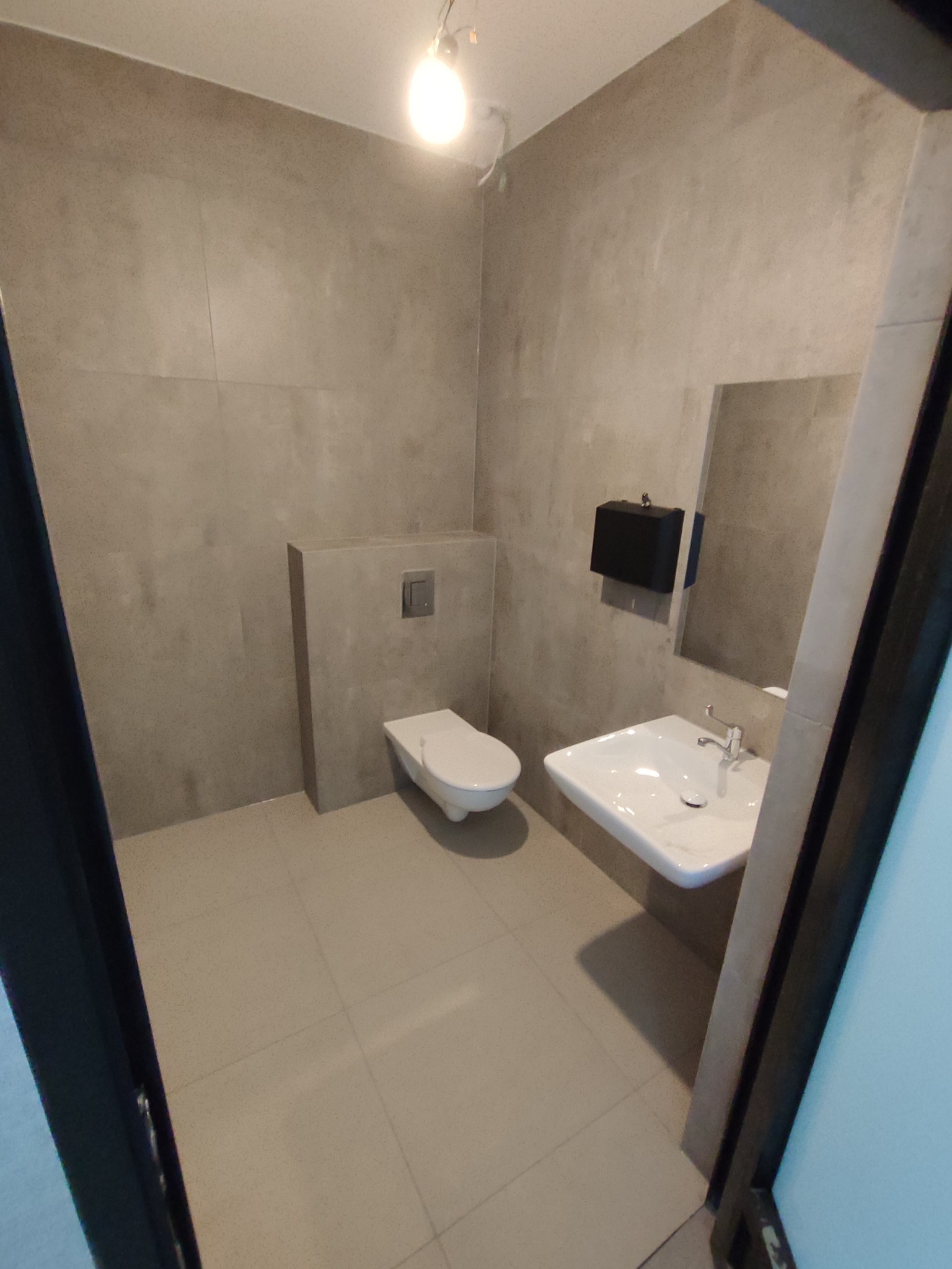 Nowoczesna łazienka w odcieniach szarości z wiszącą miską WC, umywalką i dużymi płytkami na ścianach. Minimalistyczny design, oświetlenie punktowe.