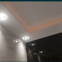 Nowoczesna łazienka z marmurowymi ścianami w odcieniach bieli i czerni, oświetlona punktowymi lampami sufitowymi i subtelnym oświetleniem LED na suficie podwieszanym.