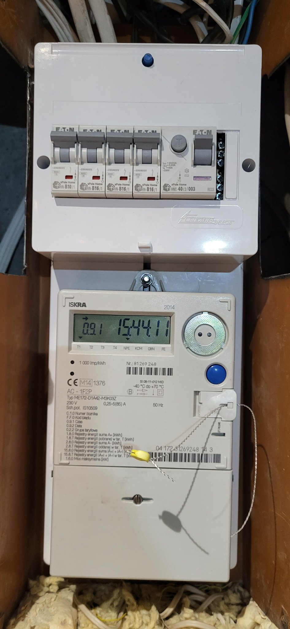 Szczegółowe ujęcie tablicy rozdzielczej z bezpiecznikami EATON i licznika energii elektrycznej ISKRA, widoczne przewody i aktualny odczyt zużycia energii.
