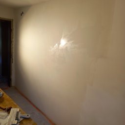 Technika Budowlana Mariusz Ogorzałek - Świeżo wyszpachlowana ściana z widocznymi śladami szpachli, przygotowana do dalszych prac wykończeniowych, z narzędziami leżącymi na stole obok