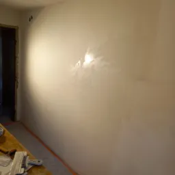 Świeżo wyszpachlowana ściana z widocznymi śladami szpachli, przygotowana do dalszych prac wykończeniowych, z narzędziami leżącymi na stole obok