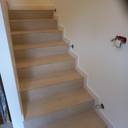 Technika Budowlana Mariusz Ogorzałek - Wykończone schody z jasnymi stopniami, białe listwy przypodłogowe, widoczne przygotowania do montażu oświetlenia na ścianie.