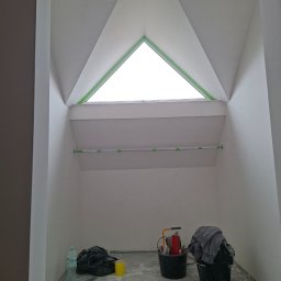 Technika Budowlana Mariusz Ogorzałek - Poddasze po szpachlowaniu w Wadowicach Górnych. Widoczne okno dachowe w kształcie trójkąta, ściany przygotowane do malowania i narzędzia pracy.