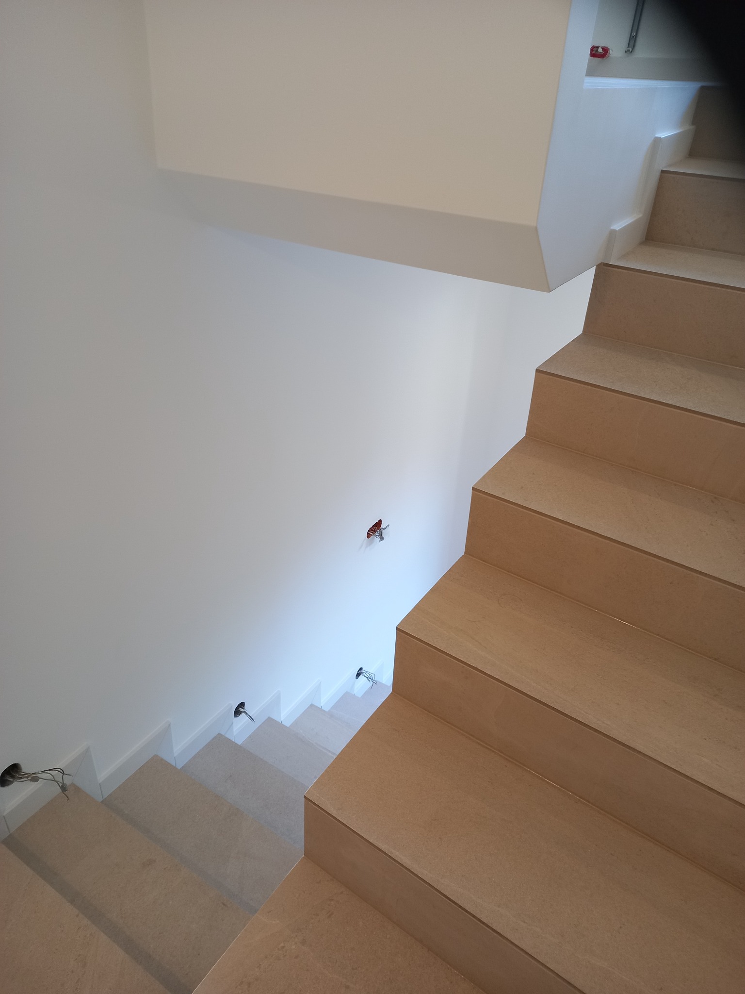 Wykończone schody wewnętrzne z okładziną z płytek imitujących drewno, widoczne punkty oświetleniowe w ścianie i na schodach. Minimalistyczny design wnętrza.