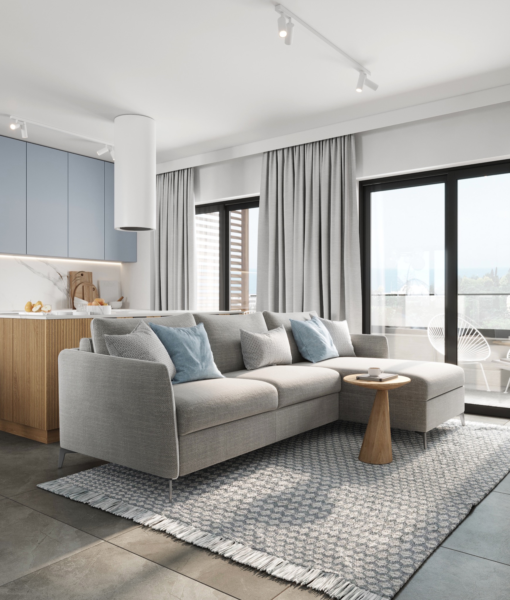 Salon z aneksem kuchennym w jasnych barwach: szara sofa narożna z błękitnymi poduszkami, okrągły stolik kawowy, dywan w geometryczny wzór, niebieskie szafki kuchenne i wyjście na balkon z białymi...