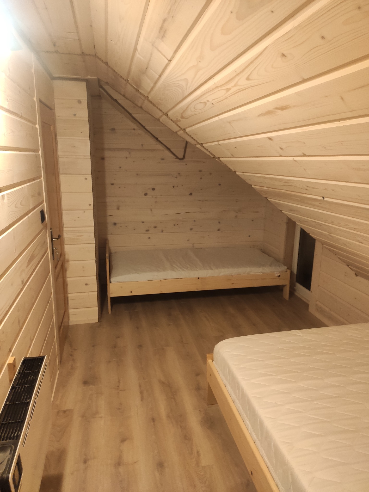 Wnętrze pokoju z poddaszem wykończonego drewnem w Tyliczu, z dwoma drewnianymi łóżkami z materacami i grzejnikiem elektrycznym przy ścianie.