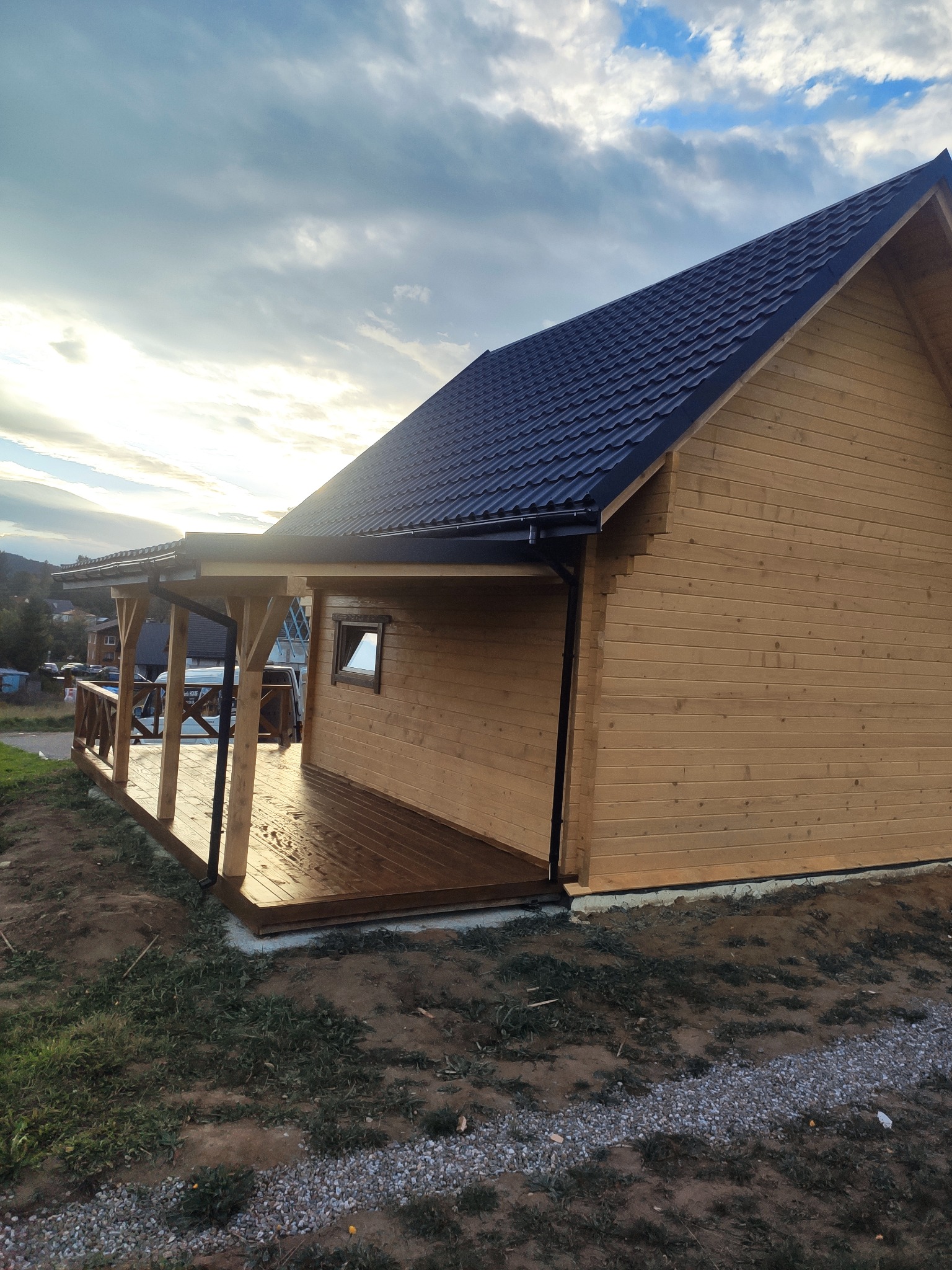 Gotowy drewniany dom z bali w Tyliczu z zadaszonym tarasem, widoczne ciemne pokrycie dachowe i drewniana elewacja.