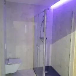 Nowoczesna łazienka z kabiną prysznicową typu walk-in z czarnym brodzikiem i podświetleniem LED w odcieniach fioletu, wisząca miska WC.