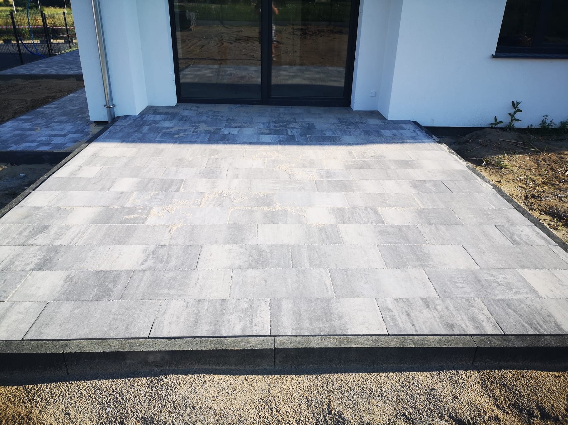 Nowoczesny podjazd z jasnoszarej kostki brukowej ułożonej przed domem w Radomiu, widoczne delikatne piaskowanie na powierzchni.