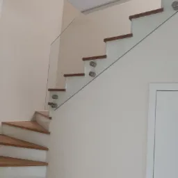 Schody drewniane z balustradą ze szkła mocowanego punktowo, widok z dołu, minimalistyczny design, jasne wnętrze.