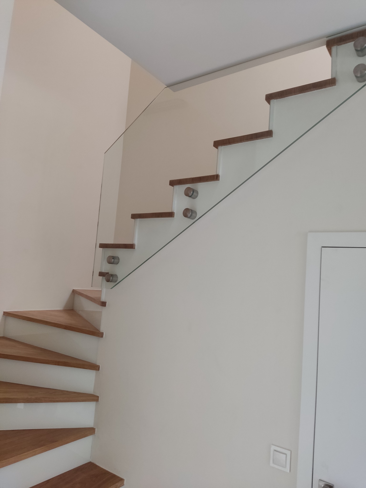 Schody drewniane z balustradą ze szkła mocowanego punktowo, widok z dołu, minimalistyczny design, jasne wnętrze.