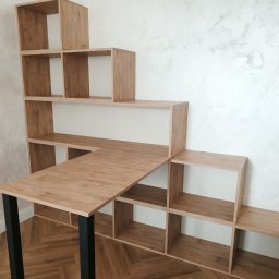 Make Me Woody Konrad Klimiuk - Kreatywna aranżacja: regał schodkowy z blatem biurka na czarnych nogach, drewnopodobny dekor, na tle ściany z efektem betonu i parkietu w jodełkę.
