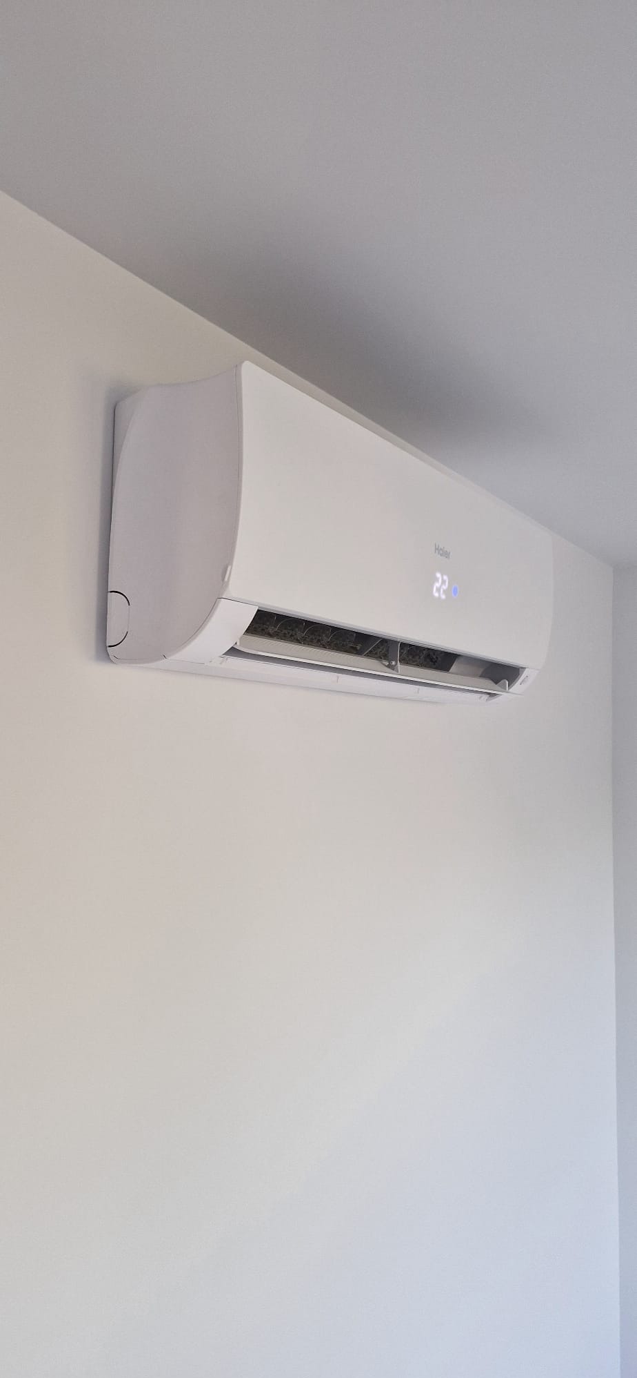 Biała klimatyzacja Haier w jasnym wnętrzu, widoczny wyświetlacz temperatury 22 stopnie, prosta forma, minimalistyczny design.