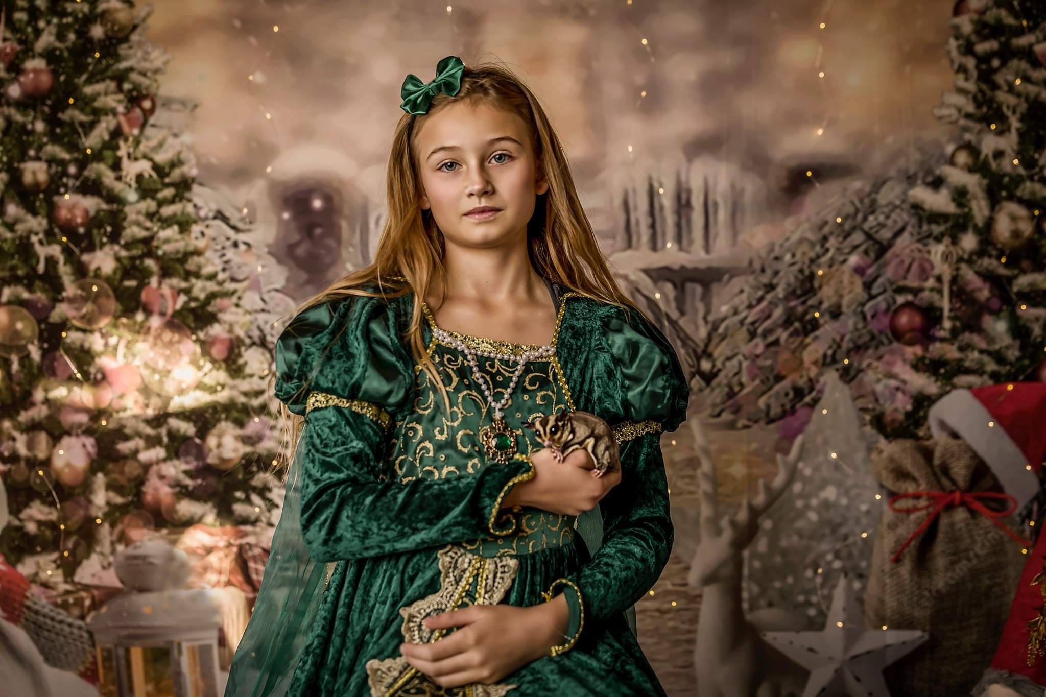 Dziewczynka w zielonej, renesansowej sukni trzymająca w dłoniach małą wiewiórkę latającą na tle świątecznej scenerii z choinką i dekoracjami.