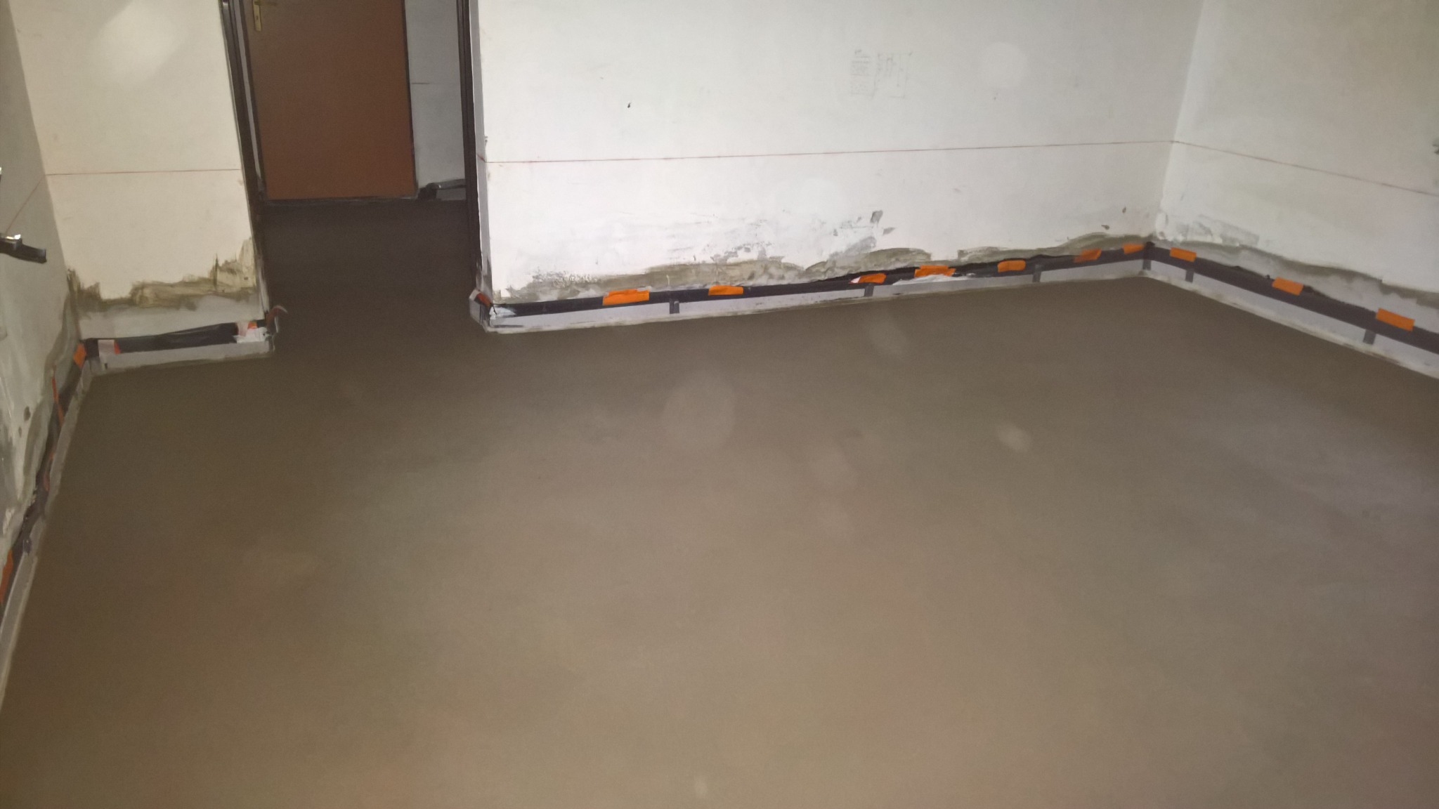 Wylany, mokry podkład podłogowy w pomieszczeniu, z widocznymi listwami dylatacyjnymi przy ścianach.