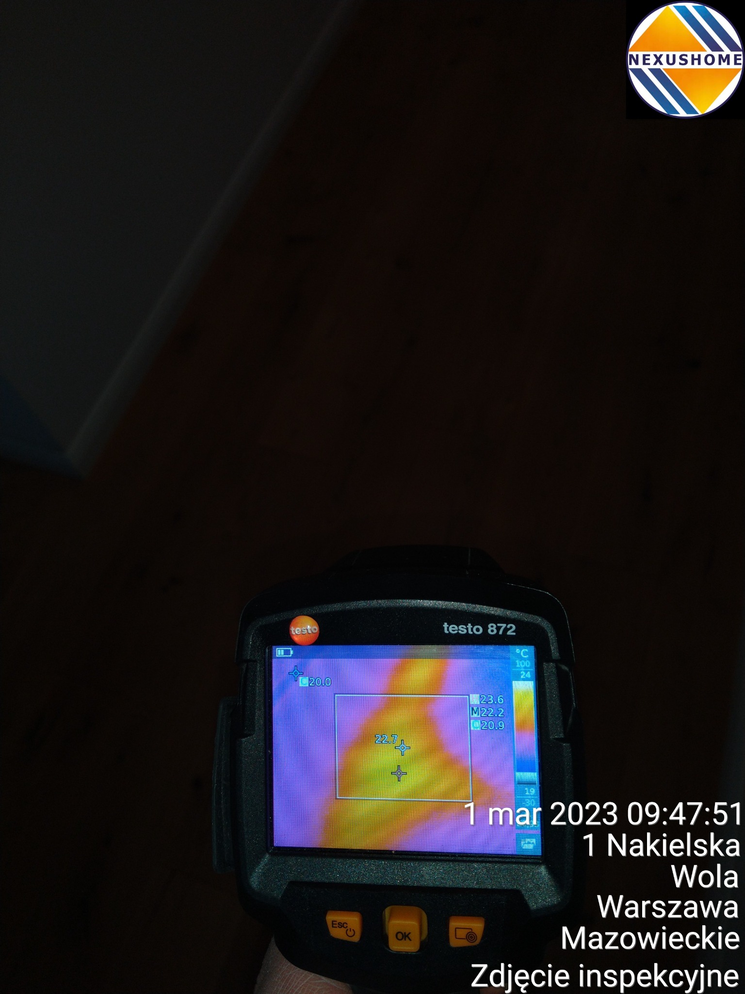 Kamera termowizyjna Testo 872 w trakcie inspekcji, wskazująca temperaturę 22.7 stopni Celsjusza, z datą i adresem na ekranie, w tle ciemna powierzchnia