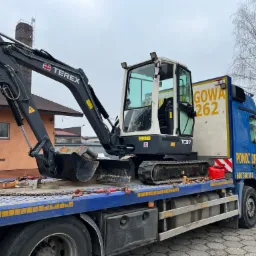 Mini koparka Terex TC37 zabezpieczona łańcuchami i pasami transportowymi na platformie lawety pomocy drogowej, widok z boku.