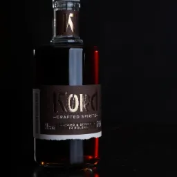 Butelka bursztynowego alkoholu Kord Crafted Spirits na ciemnym tle z refleksami światła na lakierowanym blacie.