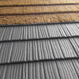 Fragment dachu z widoczną częścią pokrytą mchem i porostami, kontrastujący z wyczyszczoną, ciemnoszarą powierzchnią dachówki.