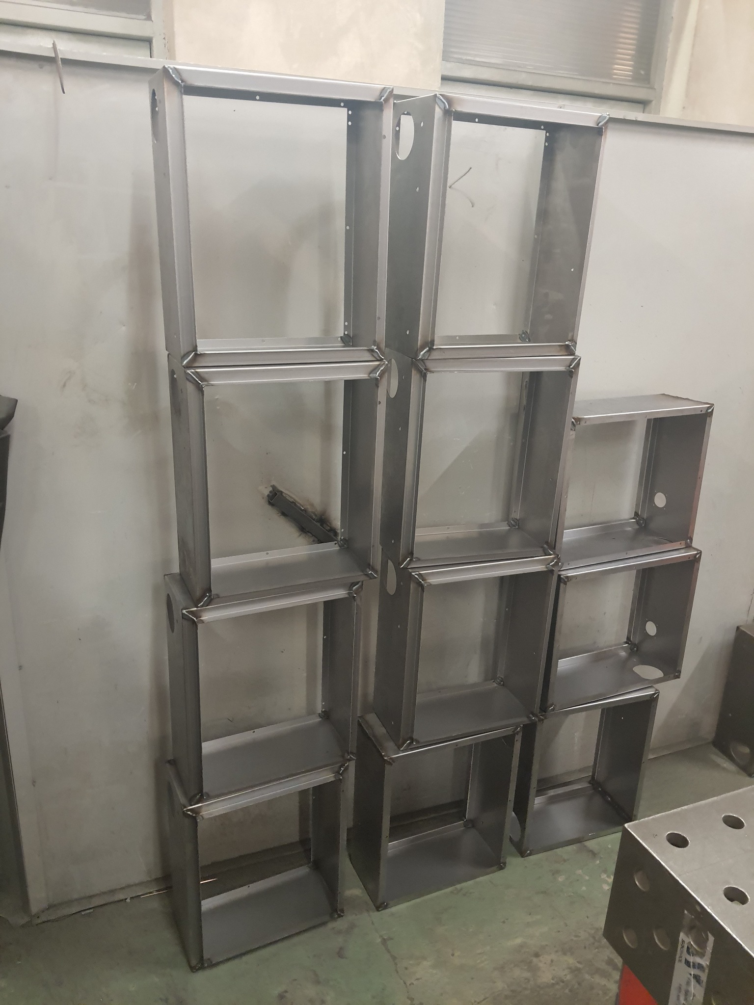 Stos metalowych, spawanych, prostokątnych obudów z otworami, ustawionych w pionie w warsztacie.