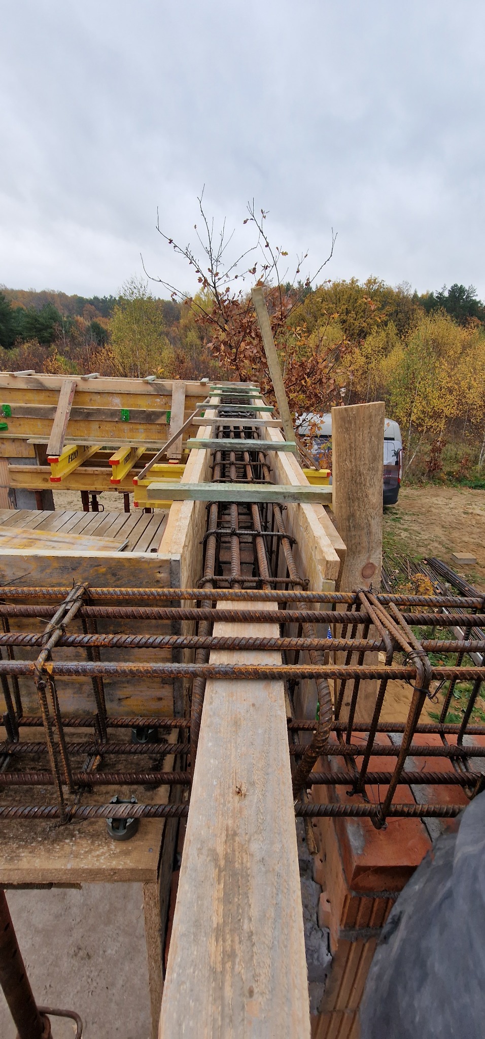 Zbrojenie fundamentu w drewnianym szalunku, widok z góry, jesienny krajobraz w tle.