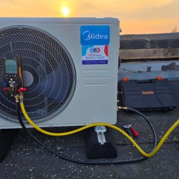 Hydro Gorzów - Biała jednostka zewnętrzna klimatyzacji Midea na dachu, podłączona do pompy próżniowej i manometru cyfrowego Testo, z zachodem słońca w tle. Widoczne narzędzia i akcesoria.
