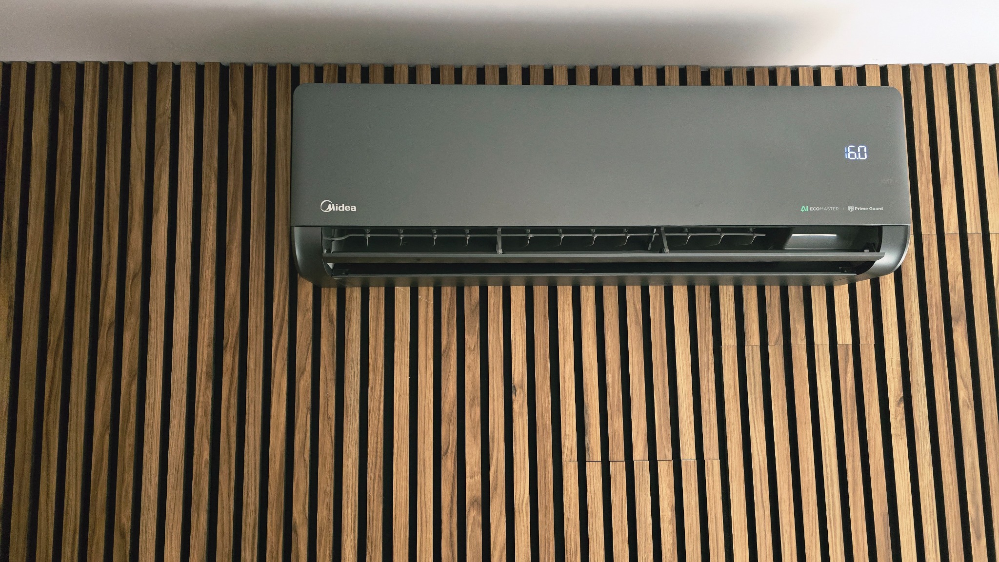 Szary klimatyzator Midea na ścianie z drewnianych listew. Widoczny wyświetlacz z temperaturą 16 stopni. Nowoczesny design, minimalistyczne wnętrze.