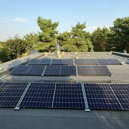 GRUPA ENERGYPRO SP. Z O.O. - Panele słoneczne zamontowane na płaskim dachu pokrytym papą, z widocznym systemem mocowań i anteną satelitarną w tle, otoczone zielenią drzew.