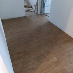 Wall Crafter Remonty ROBERT SIERSZEŃ - Ułożone panele podłogowe w odcieniach brązu w nowym mieszkaniu, widoczne materiały budowlane w tle, ściany w trakcie wykańczania.