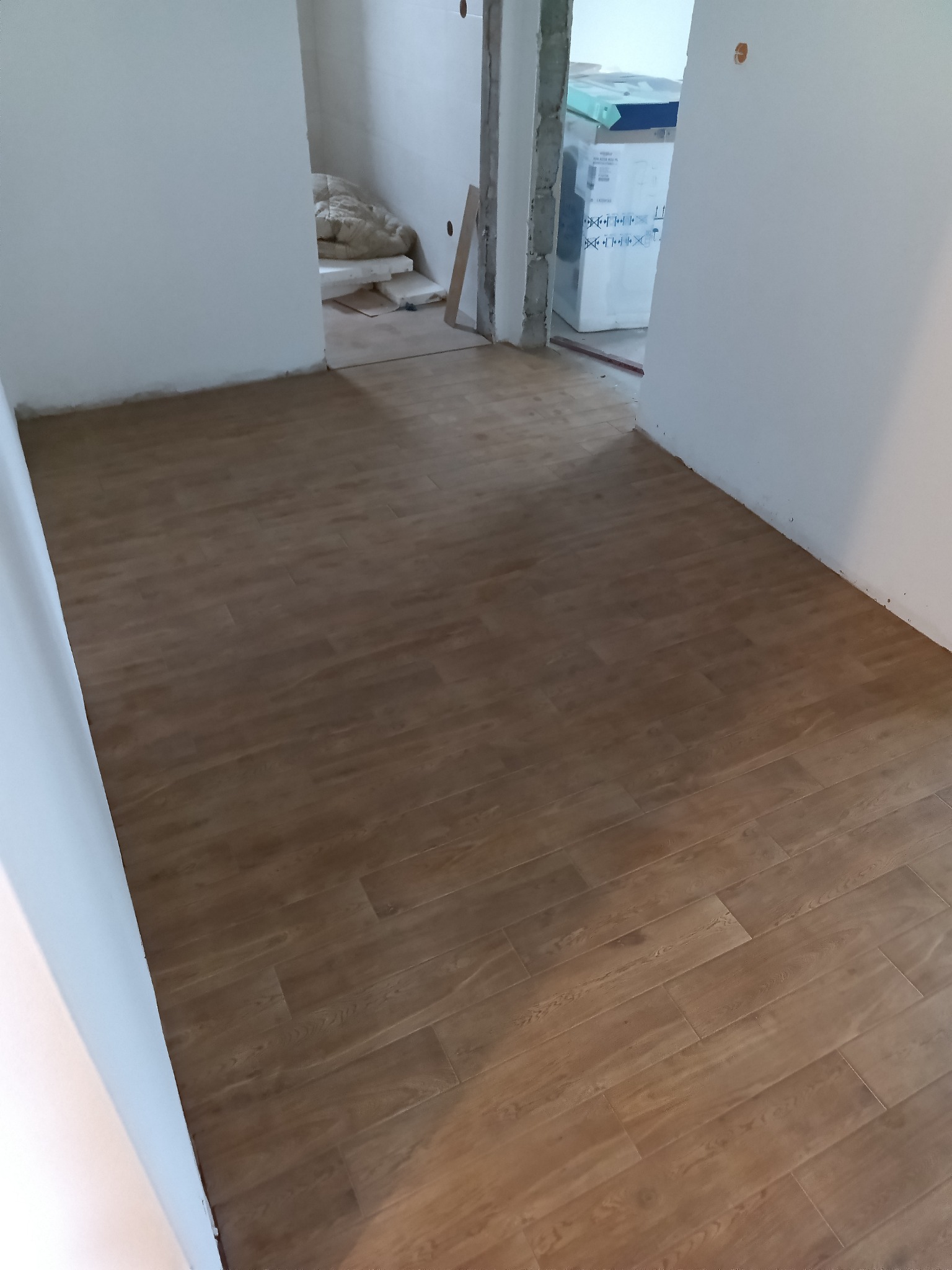 Ułożone panele podłogowe w odcieniach brązu w nowym mieszkaniu, widoczne materiały budowlane w tle, ściany w trakcie wykańczania.