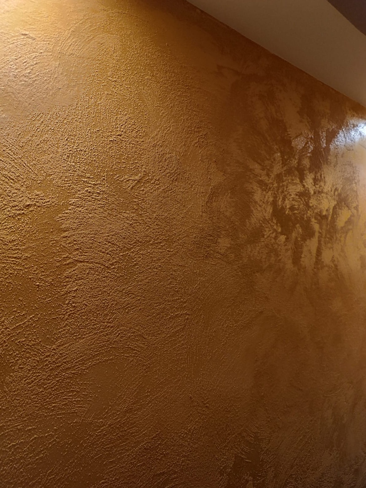 Ściana pokryta dekoracyjną farbą w odcieniach złota i brązu, z wyraźną fakturą i połyskującym wykończeniem.