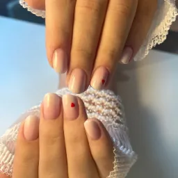 Delikatny manicure ombre w odcieniach nude z małym czerwonym serduszkiem na każdym paznokciu, dłonie ozdobione złotym pierścionkiem i koronkową rękawiczką, logo Makeup Studio w prawym dolnym rogu.