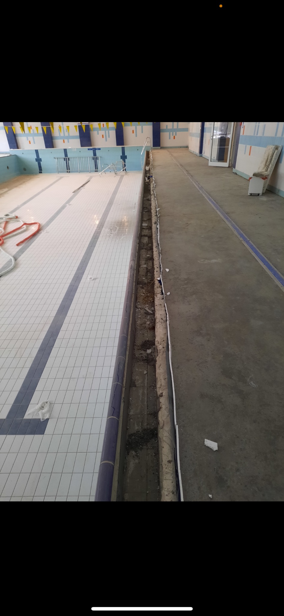 Pływalnia w trakcie remontu, widoczne usunięte płytki przy basenie, odsłonięta instalacja i betonowa posadzka.