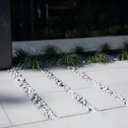 Nowoczesny taras z jasnych płyt z wąskimi pasami białych kamyków i ozdobnymi trawami, widok z góry.