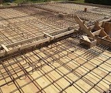 Zbrojenie płyty fundamentowej na deskowaniu z widocznymi prętami i drewnianymi elementami konstrukcyjnymi.