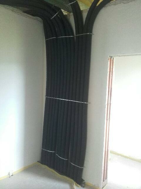 Wiązka czarnych rur instalacyjnych przymocowana drutem do ściany w narożniku surowego wnętrza podczas prac wykończeniowych.