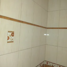 Beżowe płytki ścienne w łazience z brązowym dekoracyjnym pasem z motywem kwiatowym i pojedynczym kwadratowym elementem dekoracyjnym z kwiatami.