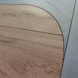 Połączenie podłogi z paneli drewnopodobnych i szarych płytek ceramicznych, widok z góry na zaokrąglone wykończenie, precyzyjne łączenie materiałów.