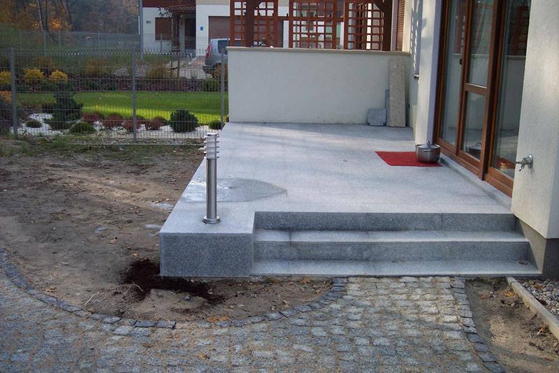 Granitowy taras z trzema stopniami, oświetleniem punktowym i brukowanym podejściem do domu.