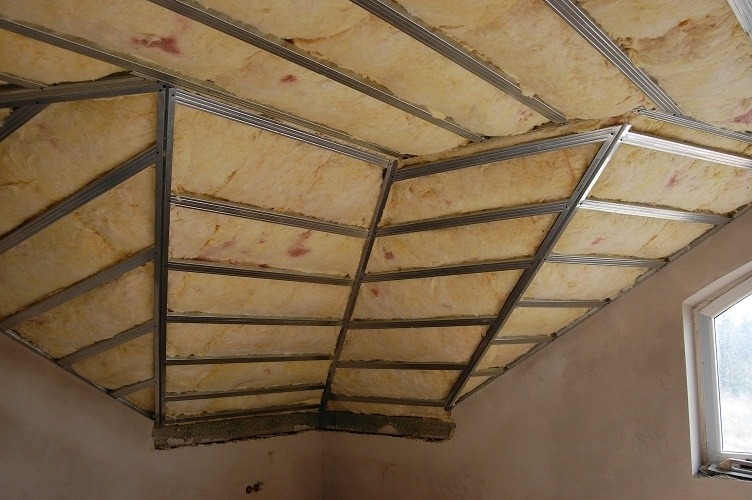 Skośny strych z widoczną konstrukcją metalową i ociepleniem z wełny mineralnej, przygotowany do montażu płyt gipsowo-kartonowych, z oknem w prawym dolnym rogu.