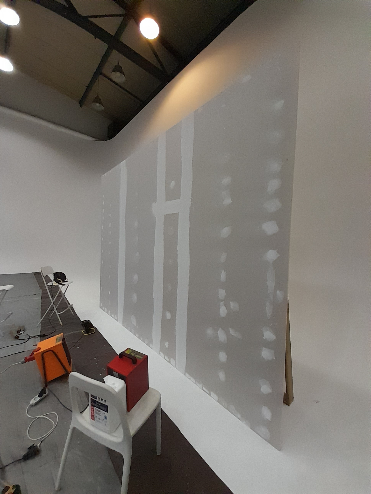 Montaż płyty karton gips na stelażu, widoczne szpachlowane łączenia i narzędzia pracy w studio fotograficznym.