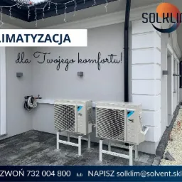 Dwa zewnętrzne agregaty klimatyzacji Daikin R32 zamontowane na białych wspornikach przed budynkiem z napisem 'Klimatyzacja dla Twojego komfortu!', widoczne logo firmy Solklim