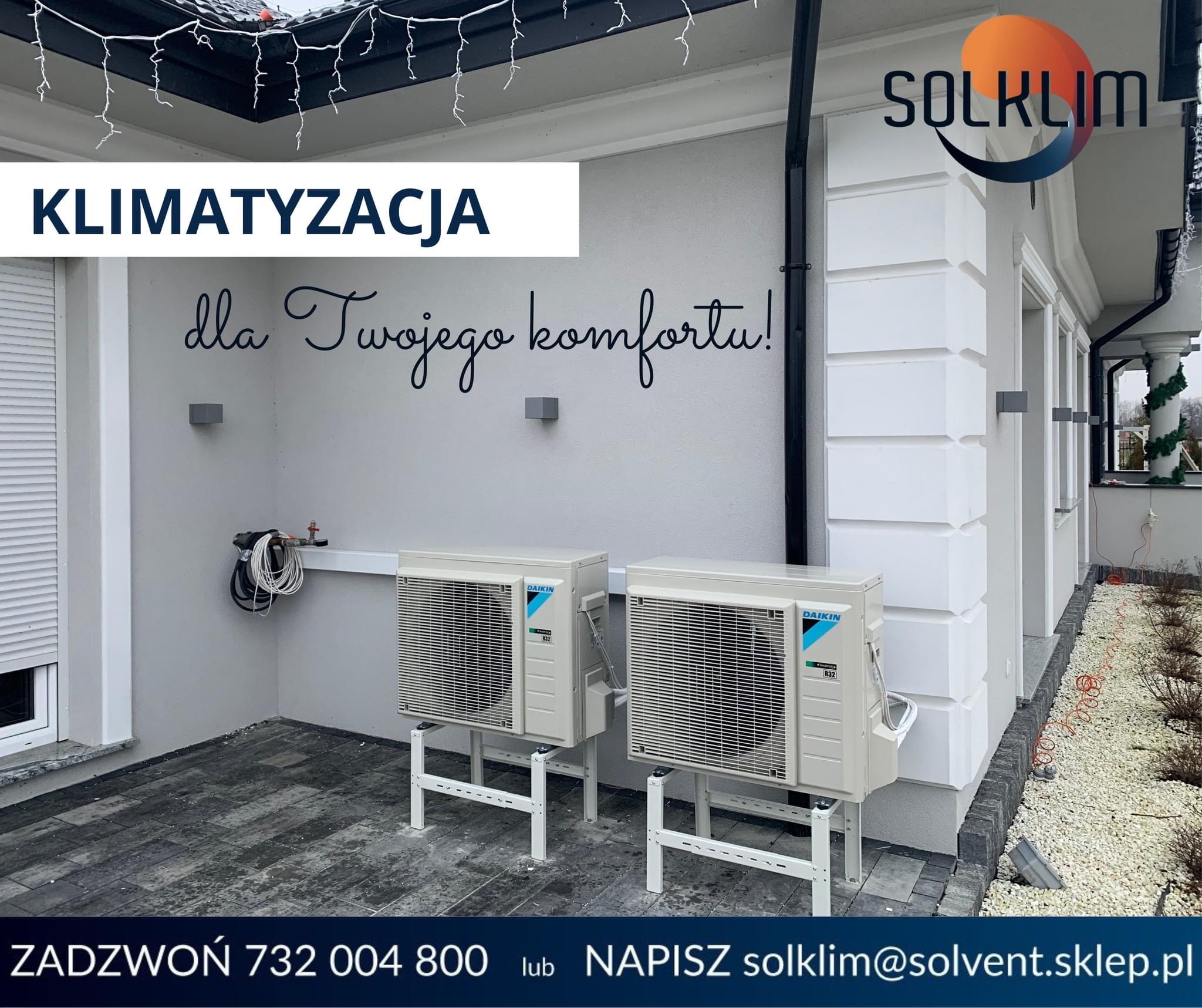 Dwa zewnętrzne agregaty klimatyzacji Daikin R32 zamontowane na białych wspornikach przed budynkiem z napisem 'Klimatyzacja dla Twojego komfortu!', widoczne logo firmy Solklim