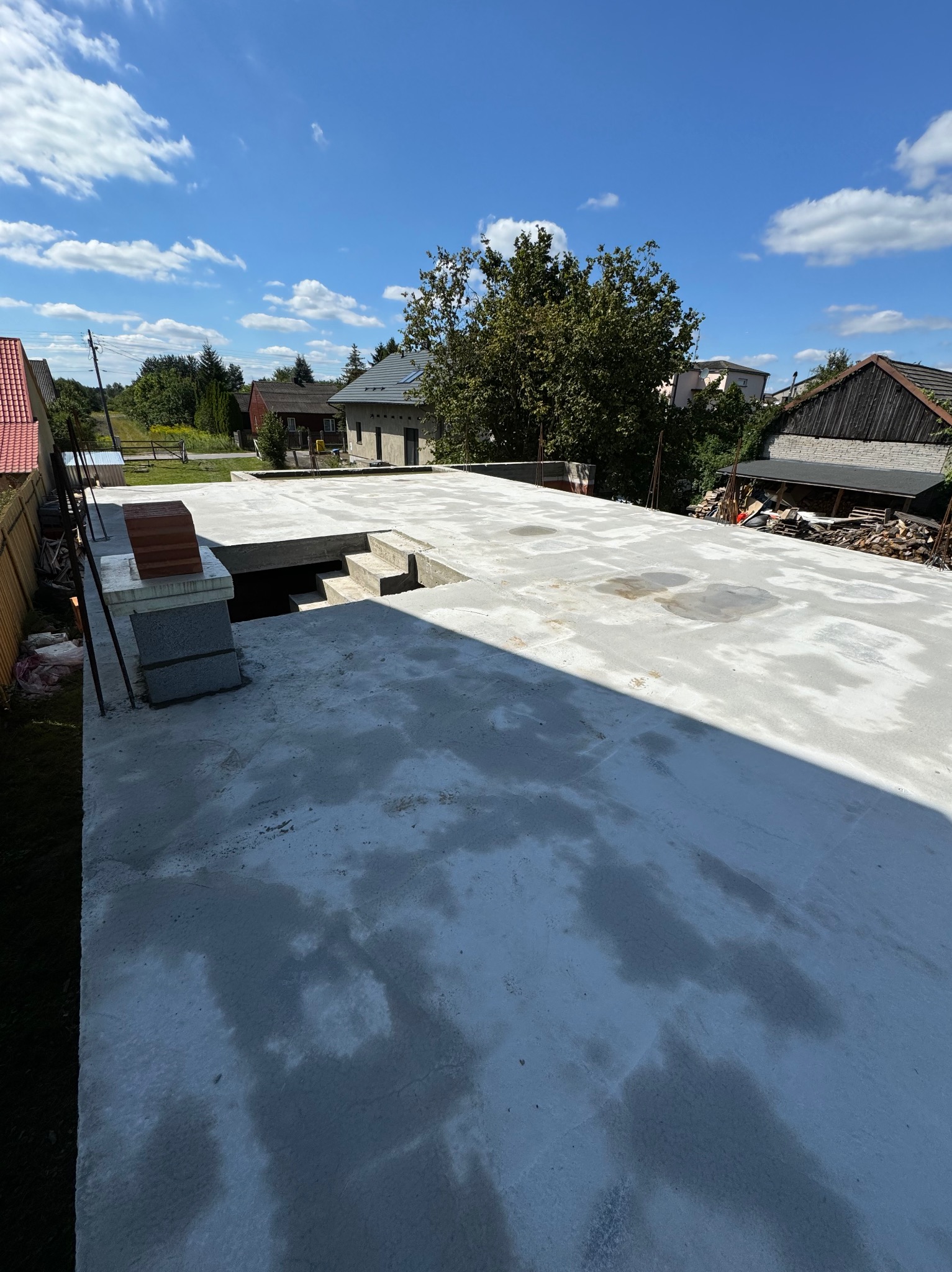 Wylana płyta fundamentowa z przygotowanym otworem na schody, widok z góry w słoneczny dzień.