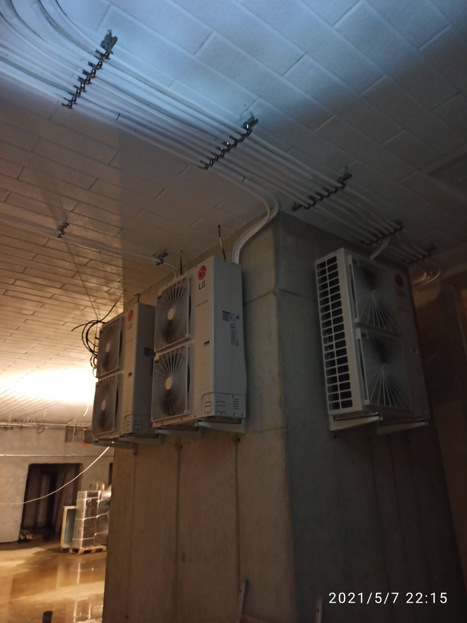 Kilka modułów klimatyzacji LG zamontowanych na betonowej ścianie w surowym wnętrzu, widoczne rury instalacyjne pod sufitem.