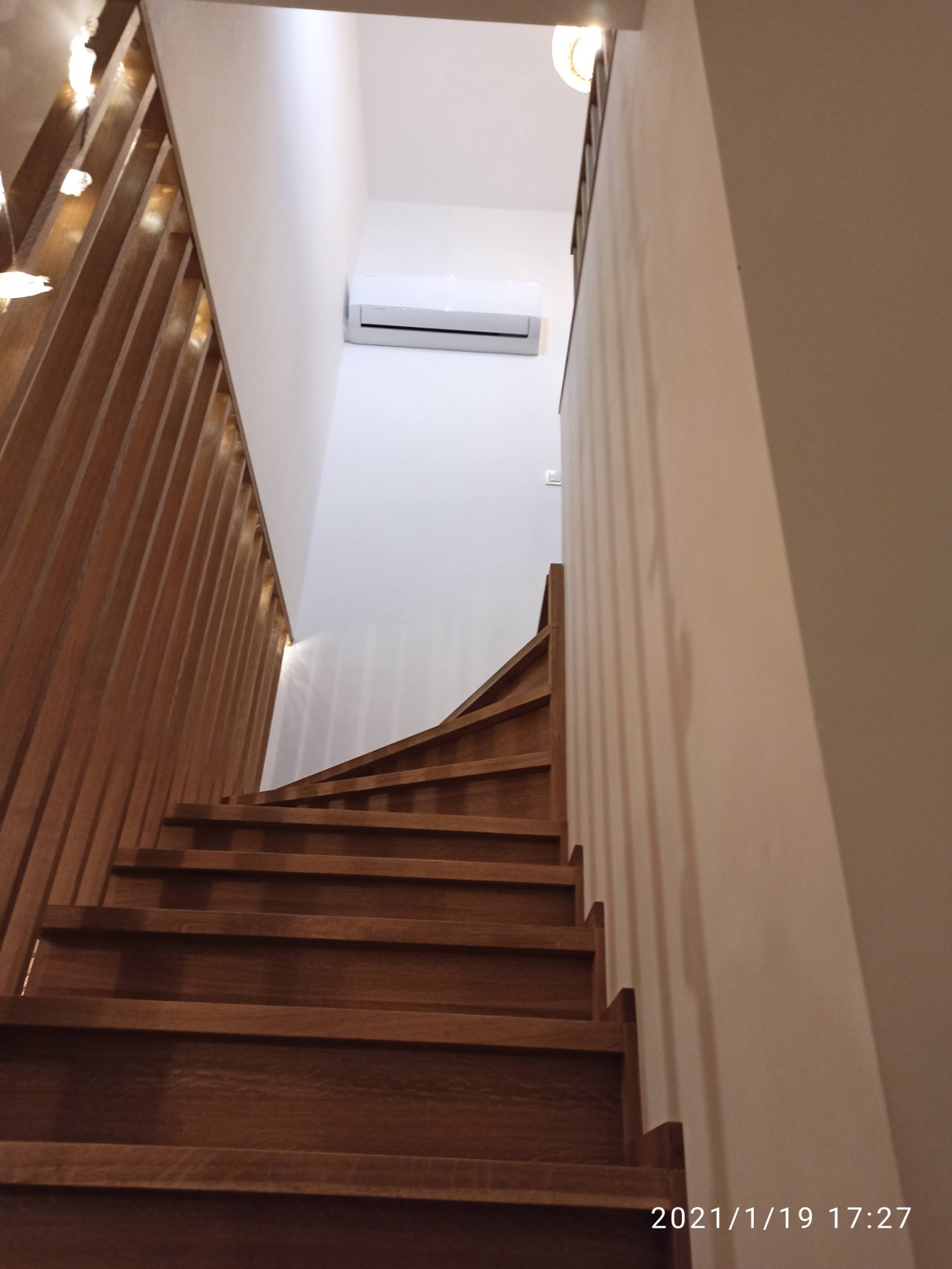 Wnętrze domu z drewnianymi schodami i zamontowaną klimatyzacją na ścianie nad nimi.